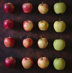 Lines of red and green apples with different shades on a brown background.