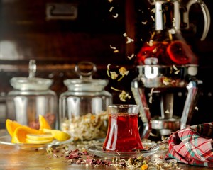 a glass of herbs tea next to lemon slices and glass tea pot
