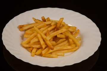 a portion of French fries on a white plate. against a black reflective surface