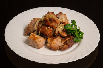 A portion of fried pork kebabs on a white plate. against a black reflective surface