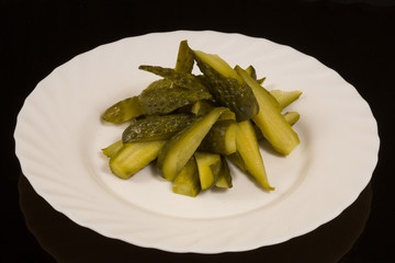 sliced pickles on a white plate. against a black reflective surface