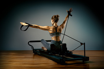 Fototapeta na wymiar The reformer simulator, the girl the Pilates trainer does exercises for stretching and shaping the correct posture on the reformer simulator. Phinness concept, correct posture, beauty and health
