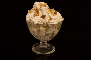 A portion of ice cream in a Cup, sprinkled with walnut crumbs. against a black reflective surface