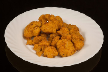 A portion of chicken breast nuggets fried in batter on a white plate. against a black reflective surface