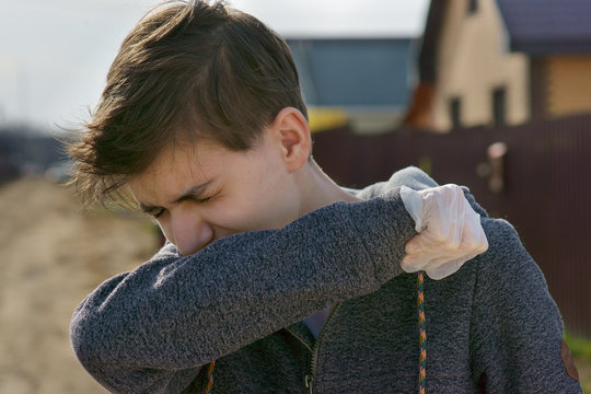 a teenager sneezes in the street, hiding behind his hand