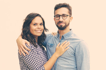 Happy satisfied family couple hugging and posing for camera. Young woman in casual and man in glasses standing isolated over white background. Relationship and affection concept
