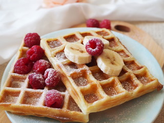Freshly baked waffles topped with powdered sugar with raspberries and bananas