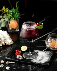 a glass of red cocktail garnished with lime zest and cranberries