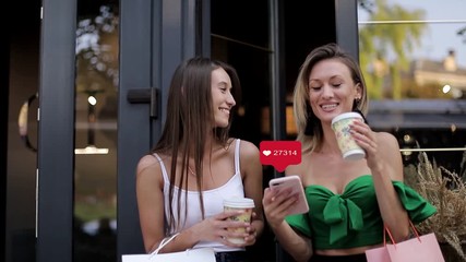Two girl friends get likes live via smartphone and social network, beautiful girls get hearts in smartphone - Powered by Adobe