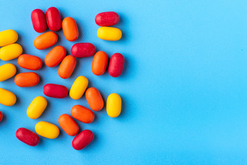 Multi-colored shiny dragees with fillings of orange, wild berries, lemon are scattered on a blue background. The view from the top.