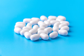 White dragees lie in a pile on a blue background. Close-up, macro photography. Lots of white mints