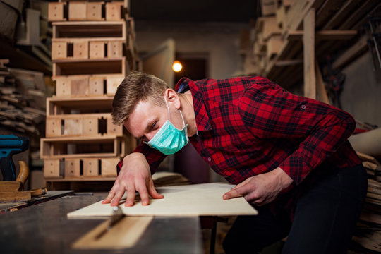 A young carpenter works in a workshop with a mask on his face
