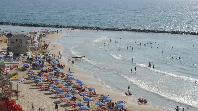  tel aviv Active sunny day with people on the beach People sunbathing on crowded beach, waves rolling onto seashore, sunny summer.