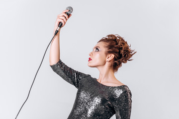 A beautiful young girl with a microphone sings on a white isolated background