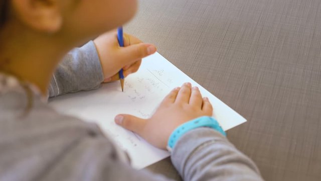 little Israeli caucasian teen gifted girl writes in a notebook in an elementary school class. She tries to solve the exercise and writing her answers on paper. OTS close up on her hands and a pencil.