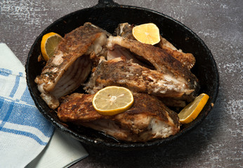 Pan with fried pieces of fish bream (Abramis) and slices of lemon close-up on a gray concrete background. Selective focus.