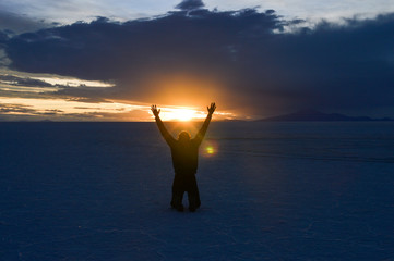 Man kneeling with arms open and raised at Salar de Uyuni in Bolivia at sunset time