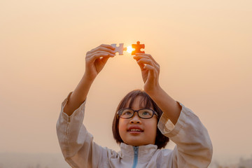 Fototapeta na wymiar Little child holding piece of blank jigsaw puzzle at sunset background