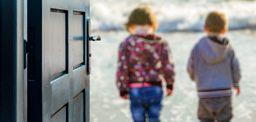 Opened door concept with two children standing by the water on the beach