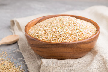Wooden bowl with raw white quinoa seeds and wooden spoon on a gray concrete  background. Side view, selective focus.