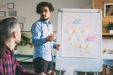 Startup leader explaining project strategy to team of coworkers. Business colleagues in casual working together in contemporary office space. Leadership or training concept