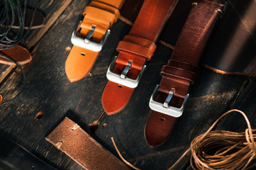 Handmade brown tone watch straps with steel buckle laying on wooden rustic surface next to leather...