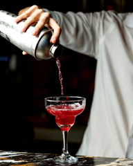 bartender pours red cocktail into a glass with long stem