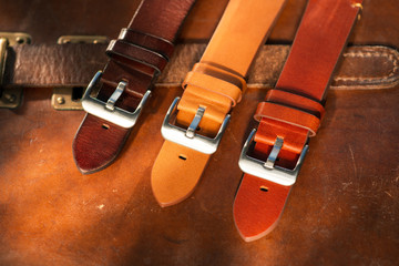 Handmade brown tone watch straps with steel buckle laying on wooden rustic surface next to leather...