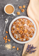 Homemade cake with milk cream, cocoa, almond, hazelnut on a black concrete  background with orange textile and a cup of coffee. Top view, copy space.