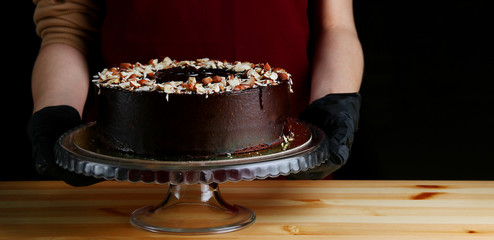 Chocolate raw cake with jam filling with hazelnuts on wooden table. vegan dessert closeup. woman confectioner hold chocolate cake with nuts. gloved hands of a pastry chef