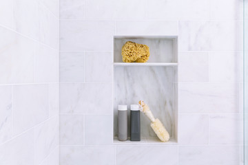 Bathroom shower interior with gray marble tile and shelves with shampoo and conditioner bottles,...