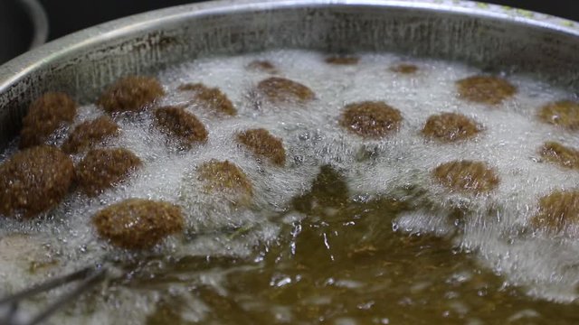 A close of a street vendor deep frying falafels in hot bubbling oil in a pan