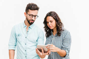 Serious focused couple reading message on tablet screen. Young woman in casual and man in glasses in glasses posing isolated over white background. Concerning news concept