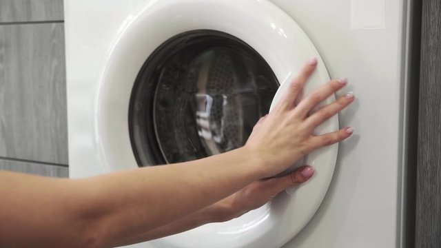 Female hand takes GREY SWEATER from laundry machine. Loading washing machine. Load clothes to washer machine. Load clothes laundry washing machine. Preparing laundry washing