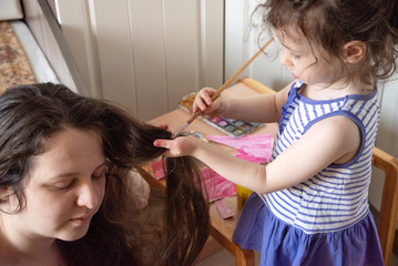 Fototapeta premium what to do in quarantine. child paints her mother s long hair with paints. Children and parents during self isolation.Mom sits on the floor, a little girl dyes her hair with watercolors. Happy family
