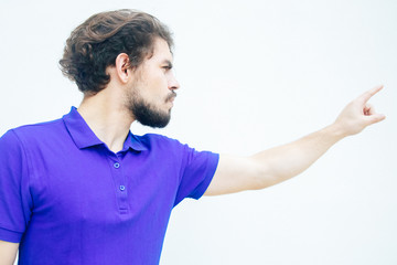 Angry displeased guy pointing finger away. Handsome bearded young man in blue casual t-shirt posing isolated over white background. Get out or fired concept