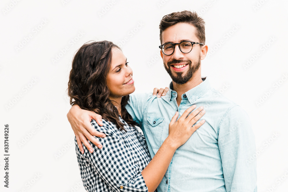 Wall mural Positive united family couple hugging, talking and posing for camera. Young woman in casual and man in glasses standing isolated over white background. Relationship and bonding concept