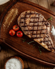 top view of beef steak with salt herbs and cherry tomato served on board