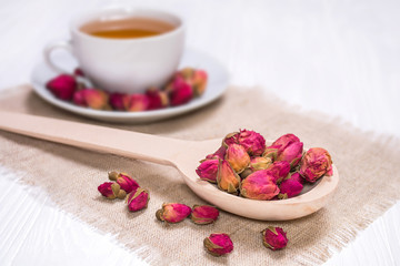 Herbal tea with rosebuds. White cup with hot tea. Wooden spoon with tea flowers