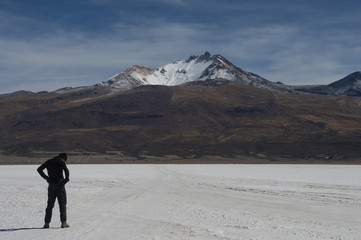 Young man with head down and hands on waist in front of the extinct Tunupa volcano in the Uyuni salt flat