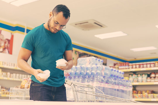 Low Angle Shot Of Smiling Man Holding Products From Freezer. Handsome Bearded Guy Shopping In Grocery Store. Shopping Concept