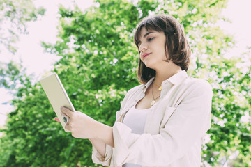 Smiling woman using tablet pc outdoors. Low angle view of cheerful young woman standing and using...
