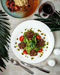 top view of grilled beef steak pieces served with vegetables and pesto sauce