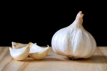 Garlic bulb and cloves on wooden table on black background..