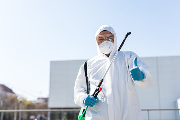 World pandemic. Disinfector in a protective suit and mask, holding disinfection chemicals outdoors