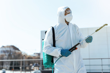 World pandemic. Disinfector in a protective suit and mask, holding disinfection chemicals outdoors