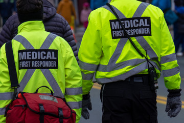 Two medical first responders walking in a street among a crowd of people.One of the EMTs is...