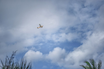 Small yellow-white plane in the clear sky with clouds.