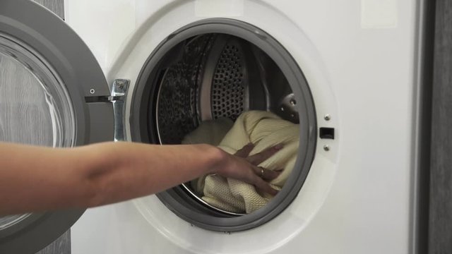 Female hand with married ring puts WHITE SWEATER in laundry machine. Loading washing machine. Load clothes to washer machine. Load clothes laundry washing machine. Preparing laundry washing