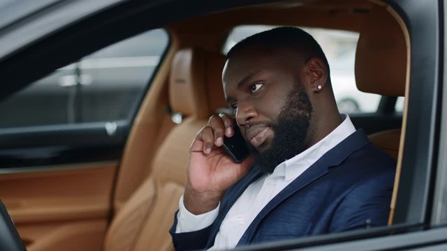 Closeup african man picking up phone at car. Man talking smartphone at car